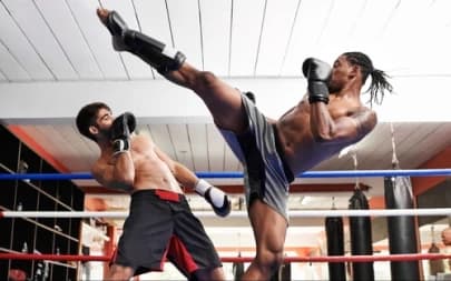 In the photo, two men are in a fighting ring, distinguished by the color of their shorts. Both are practicing kickboxing, with one attacking and the other defending.