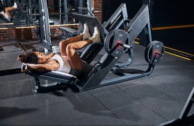 The photo is taken in a gym. A woman is doing a lower body lift exercise.