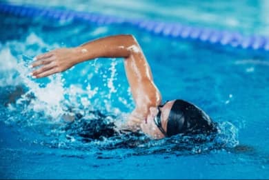 The photo is centered on a swimmer, in the pool, doing one of the swimming modalities.